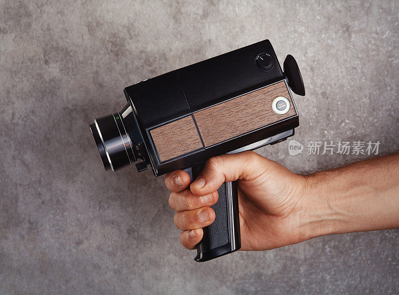 难以辨认的电影摄影师拿着老式模拟Super8, 8毫米电影摄像机在混凝土墙前。把相机对准枪